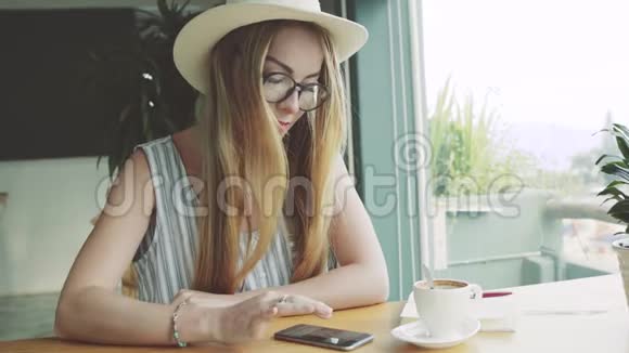 小女孩在咖啡馆里做智能手机女人用手机微笑女性创造者视频的预览图