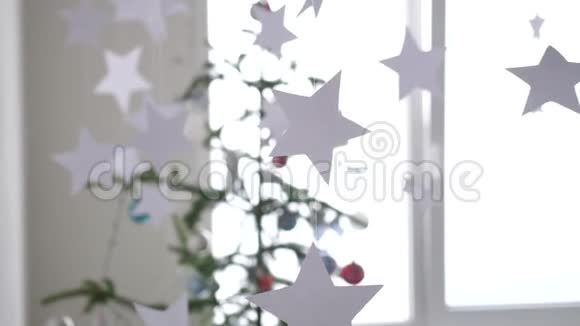 纸星星挂在窗户旁边的一棵圣诞树的前景上圣诞节的概念慢动作3840x2160视频的预览图