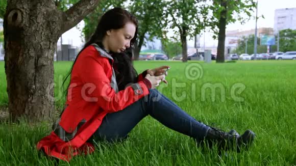 年轻女子坐在草地上发短信视频的预览图