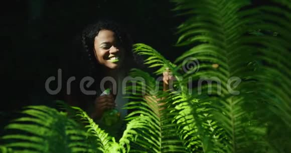 活泼开朗的美国黑人妇女的绿色成分涂着绿色的口红和眼影用蕨类植物喷洒视频的预览图
