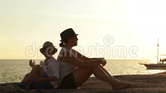 母亲和儿子在日落时坐在海滩上看着一艘船经过视频的预览图