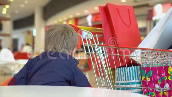 那个金发小男孩坐在购物中心的一张小桌子旁一个孩子在食品法庭的近距离射击视频的预览图