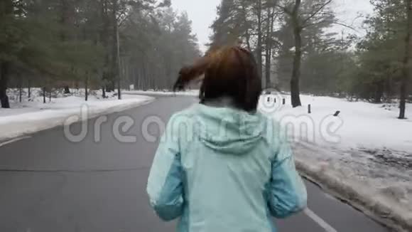 年长的白种人女人戴着耳机在冬天的雪地公园里跑步后面跟着视频的预览图