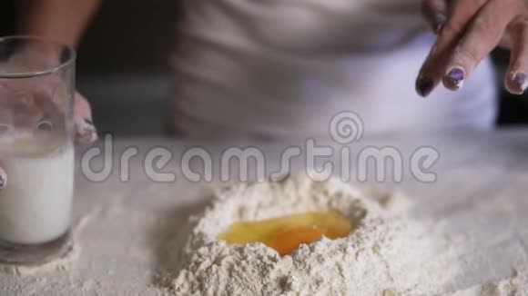 在厨房桌子上用鸡蛋将牛奶从玻璃中添加到面粉中的女性手的特写镜头慢镜头视频的预览图