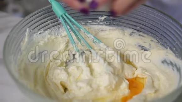 在厨房里用搅拌器将鸡蛋和其他配料混合在一起的女性手的特写镜头自制视频的预览图