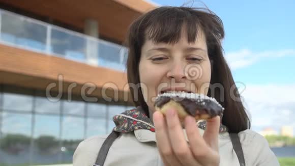 在街上吃巧克力甜甜圈的年轻女子视频的预览图