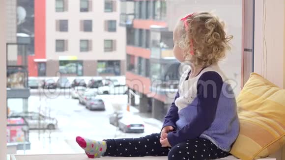 淘气的女孩戴着太阳镜坐在靠近窗户的散热器上下雪了视频的预览图