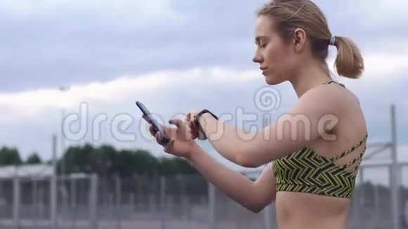 穿着健身服的女人检查手机和健身手镯视频的预览图