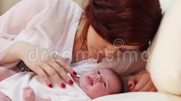 年轻的妈妈在白色的床上抚摸她可爱的小宝宝视频的预览图