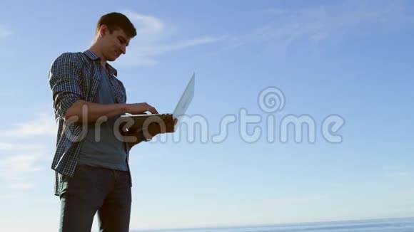 一个开朗的年轻人正在海边和他的朋友聊天用他的笔记本电脑视频的预览图