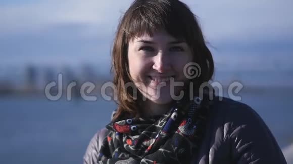 一位年轻可爱的微笑女人在冬季河流背景上的肖像视频的预览图