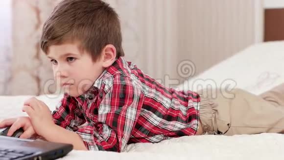 小男孩使用笔记本电脑聪明的孩子躺在床上玩电脑网络游戏电子设备视频的预览图