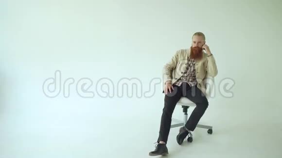 坐在旋转的办公椅上看着白色背景下的摄像机一个长着胡子的严肃男人视频的预览图