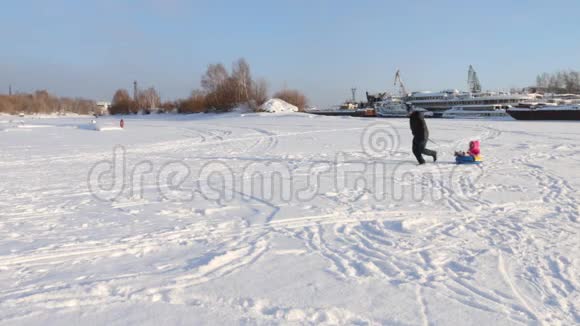 快乐的父亲把他的小女儿卷在船附近结冰的河上的雪管上视频的预览图