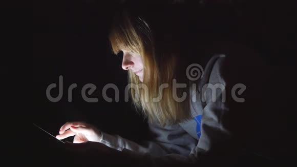 年轻漂亮的金发女孩用平板电脑躺在床上熄灯视频的预览图