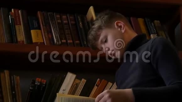 十几岁的男孩在图书馆里阅读一本书背景是书架上有很多书视频的预览图