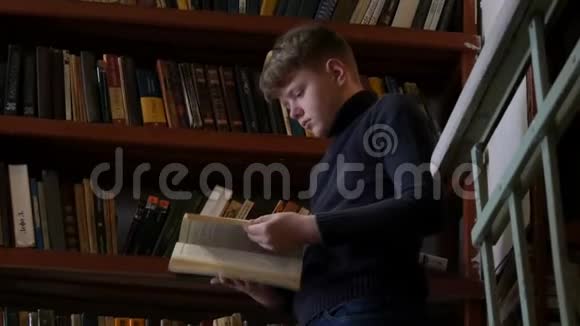 十几岁的男孩在图书馆里阅读一本书背景是书架上有很多书视频的预览图