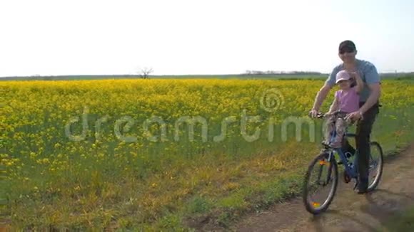 骑自行车的人带着孩子爸爸和一个女儿骑自行车带着油菜的田野健康的生活方式视频的预览图