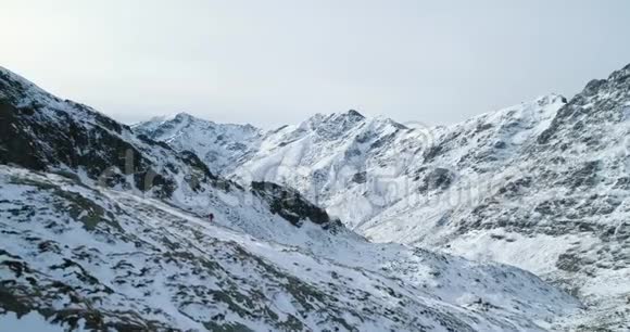 侧航越冬雪山口与登山滑雪者上行攀登白雪覆盖的群山视频的预览图