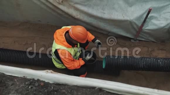 戴橙色安全帽的工人坐在沟里用黑色塑料管抹油视频的预览图