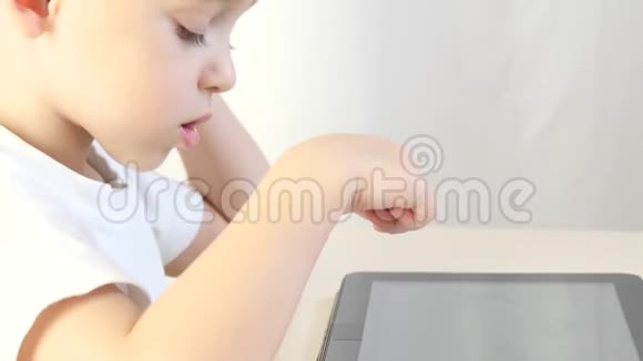 快乐的孩子坐在桌子旁玩平板电脑特写孩子在玩电子游戏因特网和视频的预览图