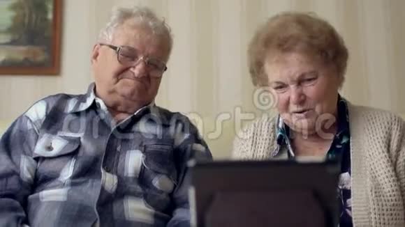 高级夫妻在沙发上使用电子标签一对快乐的老夫妇在数码平板电脑上视频聊天视频的预览图