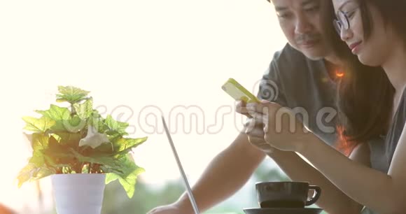 快乐的亚洲男人和女友一起使用手机和笔记本电脑视频的预览图