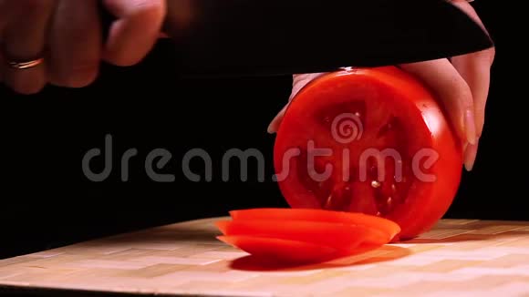 女性手特写在黑色背景下的切板上拿起刀和成熟番茄片视频的预览图
