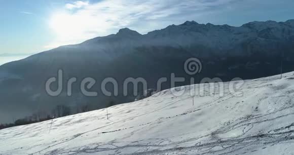 在阳光明媚的日子里带着云的滑雪道在冬季雪山上向后俯视白色背景阿尔卑斯山视频的预览图
