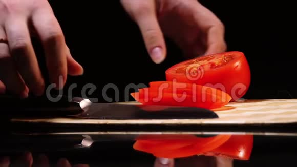 女性手特写在黑色背景下的切板上拿起刀和成熟番茄片视频的预览图