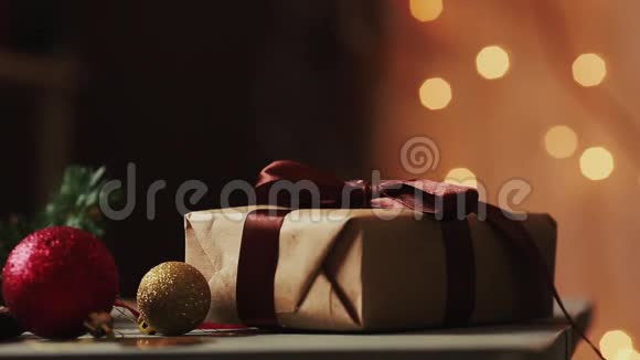 特写在圣诞灯光的背景下女性双手打开牛皮纸上的礼物背景模糊不清视频的预览图