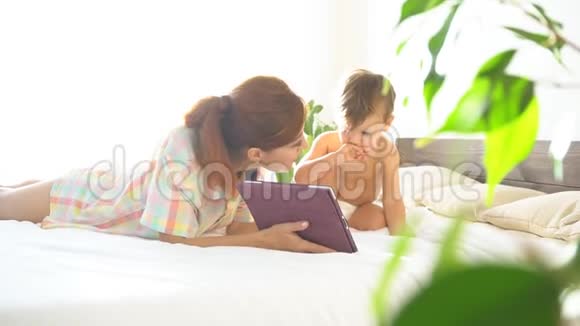 母亲和年幼的儿子躺在床上用平板电脑上网视频的预览图