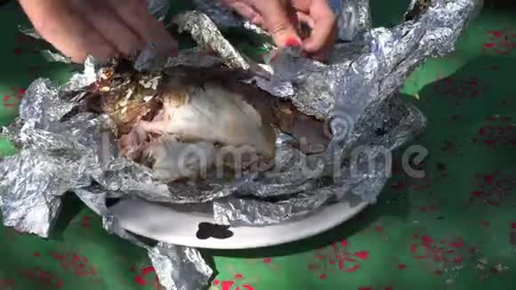 女性的手打开新鲜的鱼在室外壁炉的余烬中用箔片烤4K视频的预览图