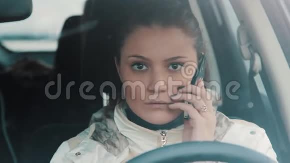 年轻的黑发女人坐在车里用手机说话下雪视频的预览图
