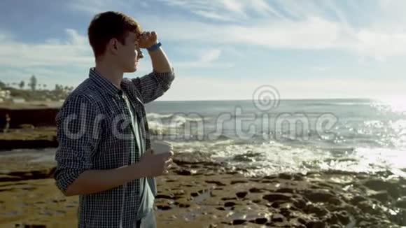在海滩上喝咖啡的时候帅哥在远处看视频的预览图