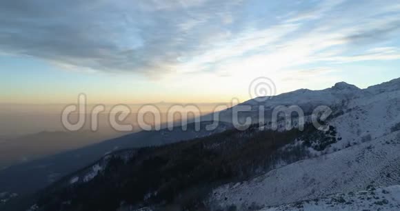 在日落或日出时侧面俯瞰冬季雪山和森林黄昏或黎明视频的预览图