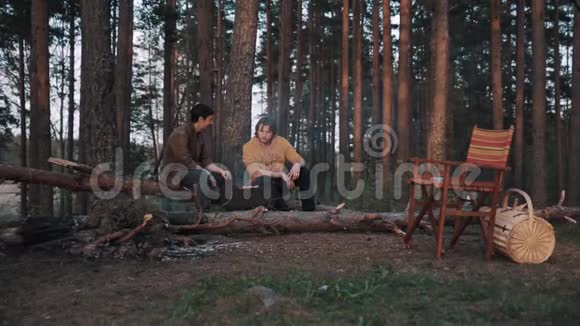 两个男朋友坐在树林里的木头上做烧烤聊天视频的预览图