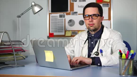 穿着白色外套的医生坐在柜子里在他的笔记本电脑上工作视频的预览图
