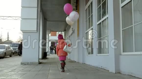 早春一个小女孩带着五颜六色的气球走在城里的一条街上视频的预览图
