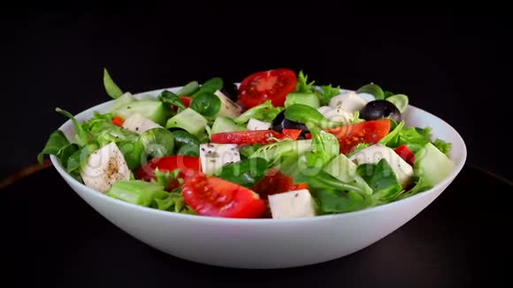 健康的饮食蔬菜沙拉和奶酪西红柿和黄瓜片板在黑色背景上旋转视频的预览图