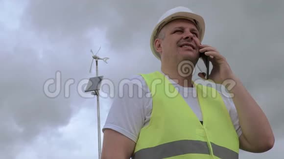 工程师在带太阳能电池板的风力发电机附近用智能电话交谈视频的预览图