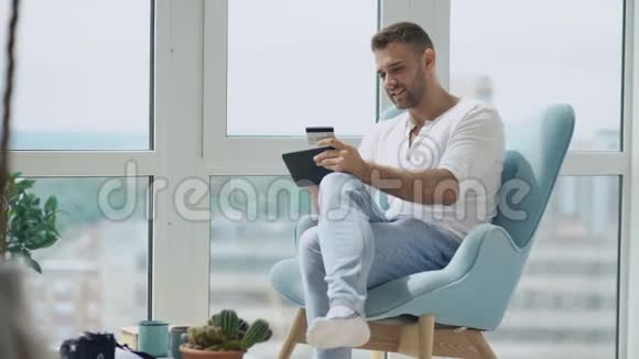 年轻的微笑男用数码平板电脑在现代阁楼公寓的阳台上购物视频的预览图