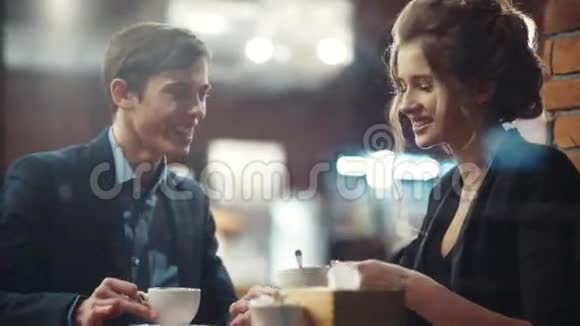 年轻的幸福夫妇交谈喝咖啡笑着约会他在智能手机上显示照片视频的预览图