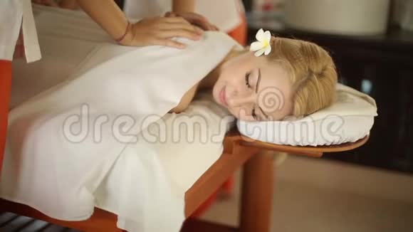 在异国情调的度假胜地的水疗床上为美丽的女人提供贴身服务漂亮的金发女孩放松和按摩与花在视频的预览图