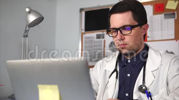 男医生穿着白色外套听诊器在他的笔记本电脑上工作视频的预览图