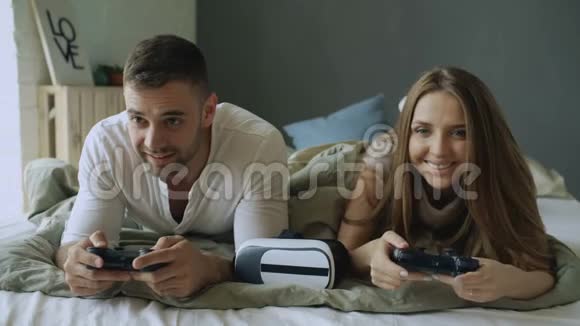 年轻夫妇在家里躺在床上玩电子游戏视频的预览图