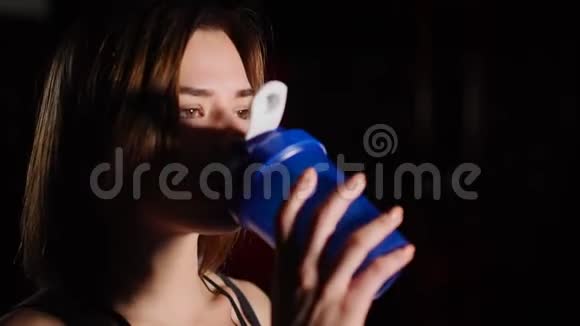 漂亮的年轻女人脖子上有一条毛巾在健身房里喝着瓶子里的水视频的预览图