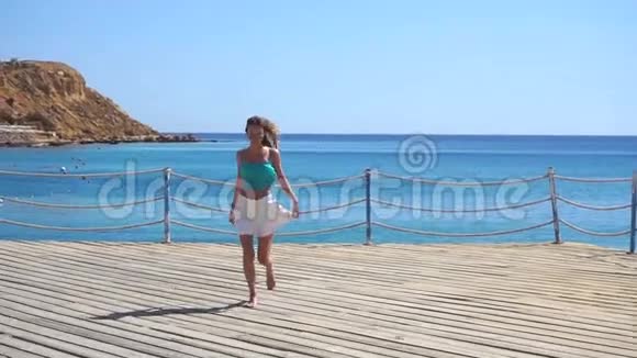 一个留着长发和眼镜的女孩慢吞吞地在靠近蓝海的码头上奔跑视频的预览图