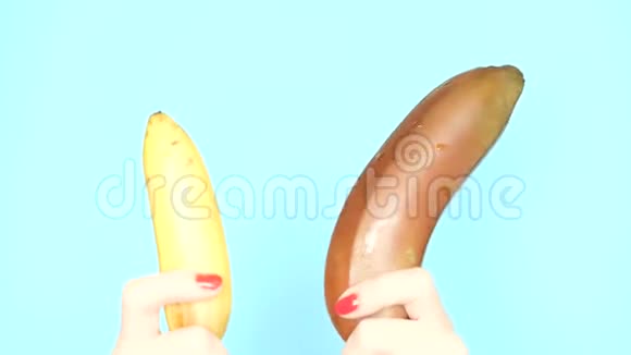 戴着红色指甲的女性手拿着一根红色香蕉和一根蓝色背景的黄色香蕉视频的预览图