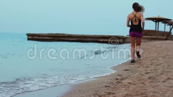那个运动女孩沿着海浪翻滚的沙滩奔跑布鲁内特早上在海岸线上慢跑视频的预览图